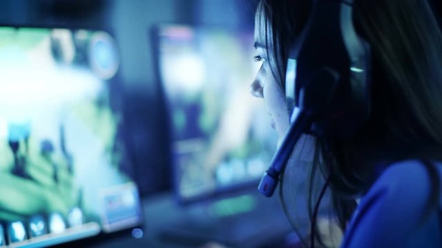 Professional Girl Gamer Plays in MMORPG/ Strategy Video Game on Her Computer. She's Participating in Online Cyber Games Tournament, or in Internet Cafe. She Wears Gaming Headphones. 4K UHD.