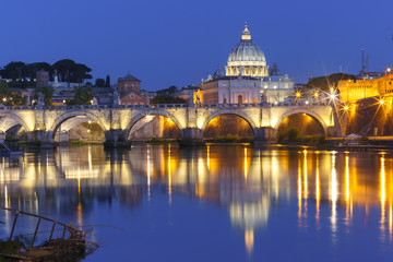 Fototapeta na wymiar Saint Angel bridge and Saint Peter Cathedral with a mirror reflection in the Tiber River during morning blue hour in Rome, Italy.
