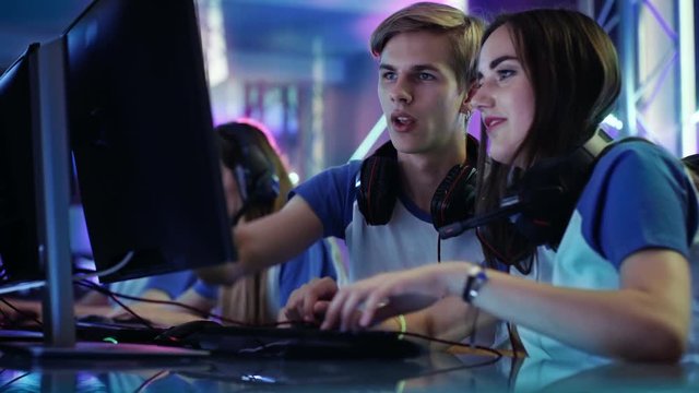 Boy and Girl Gamers Actively Thinking/ Discussing Game Strategy/ Tactic, They're In Internet Cafe or on Cyber Games Tournament. Shot on RED EPIC-W 8K Helium Cinema Camera.