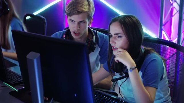 Boy and Girl Gamers Actively Thinking/ Discussing Game Strategy/ Tactic, They're In Internet Cafe or on Cyber Games Tournament. Shot on RED EPIC-W 8K Helium Cinema Camera.