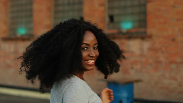 Portrait of beatiful curly hair african woman walking on the roof. View from the back.