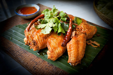 Deep fried chicken wing with fishsauce and fried onion and chilly, eat with chilly sauce. Thai dish on thai table set.