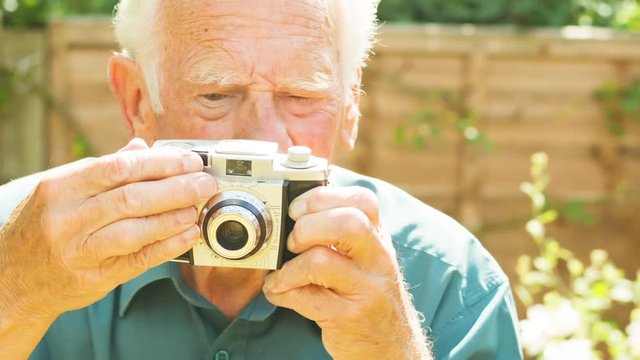 Portrait of an active Senior Caucasian man taking photos with an old film camera in his garden themes of photography hobbies retirement nostalgia analogue