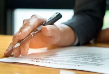 Businessmen holding pens in hand reading documents on the desk,Businessmen holding pens in hand reading contract documents before signing.