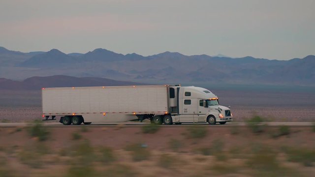 CLOSE UP: Freight semi truck driving and transporting cargo container on empty highway, delivering goods