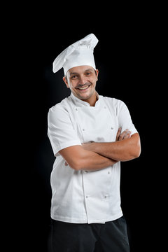 Chef Wearing Uniform With Black Pants And White Hat Isolated On A Black Background Smiling 