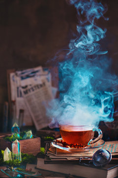 Steaming glass cup of tea with herbs and berries in a magical still life with moss and crystals.