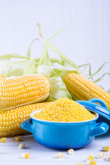 Corn grits polenta in a blue ceramic bowl on white table with ripe raw corn cob and green leaves
