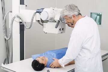 Fototapeta na wymiar Male Doctor Adjusting X-ray Machine Over Patient In Hospital