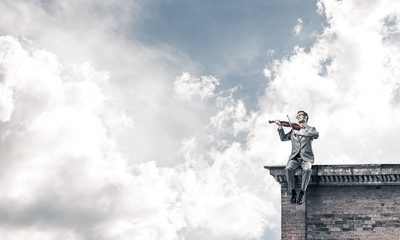 Handsome violinist in glasses on building edge play his melody
