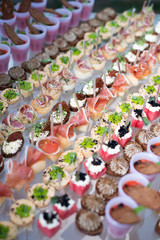 Different canapes with smoked salmon, cucumber and red currant served on sea shell over a mirror plate. Pastry cream cheese and cucumber canapes. Gorgonzola and olives Small catering canape