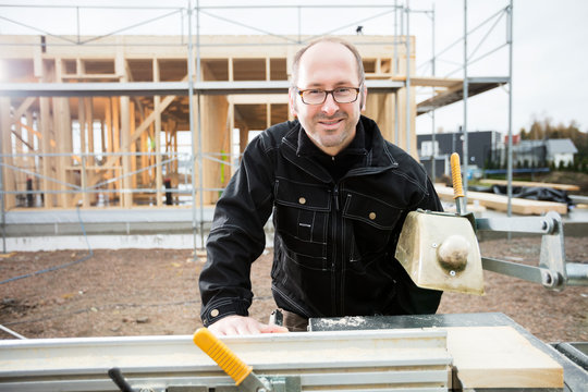 Male Carpenter Smiling While Using Table Saw To Cut Plank