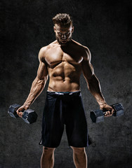 Fototapeta na wymiar Young guy working out with dumbbells. Photo of strong male with naked torso on dark background. Strength and motivation.