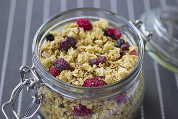 Bowls of  granola  with dry raspberries, cranberries and blueberries on marble table.