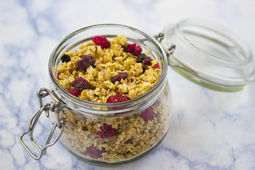 Bowls of  granola  with dry raspberries, cranberries and blueberries on marble table.