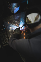 Metallurgy industry. Factory for production of heavy pellet stoves and boilers. Close up of manual worker welder on his job. Extremely dark conditions and visible noise.