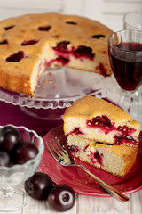 Homemade plum cake on a glass stand and red wine.