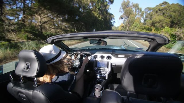 Blond model girl is driving in convertible car in white hat in California having her hair waving in the wind