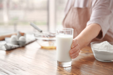 Old woman holding glass with fresh milk on table