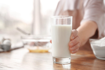 Old woman holding glass with fresh milk on table