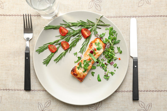 Plate with salmon, herbs, glass and flatware on light table