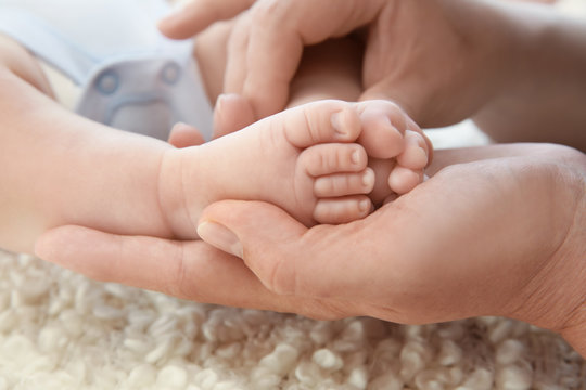 Young mother holding feet of little baby, closeup