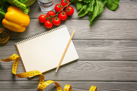 Empty notebook, measuring tape and set of healthy food on wooden table