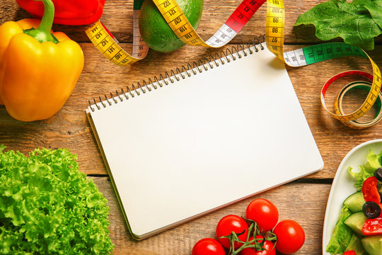 Empty notebook, measuring tape and set of healthy food on wooden table