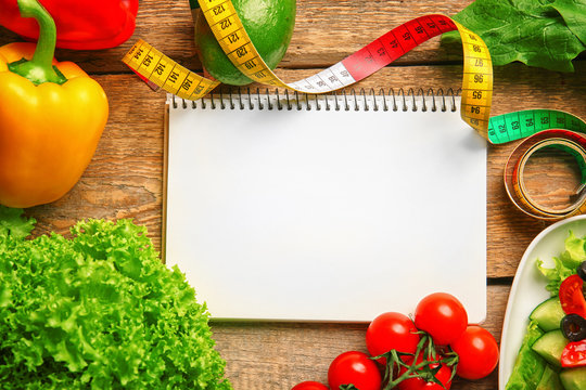 Empty notebook, measuring tape and set of healthy food on wooden table