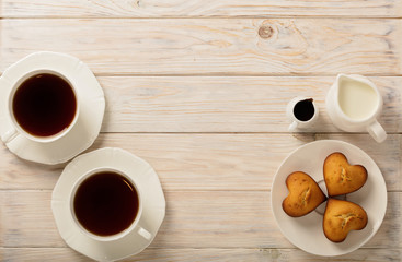 Cups with tea and cupcakes in the shape of a heart on a light wooden background.