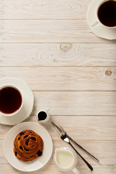 Cups with tea and biscuits on a light wooden background.