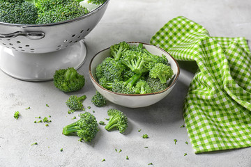 Bowl and colander with fresh green broccoli on table