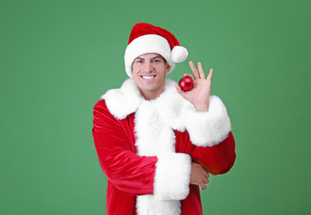 Handsome man in Santa Claus costume holding shiny bauble on light background