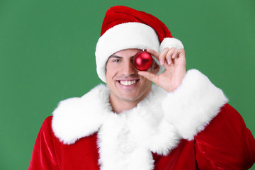 Handsome man in Santa Claus costume holding shiny bauble on light background