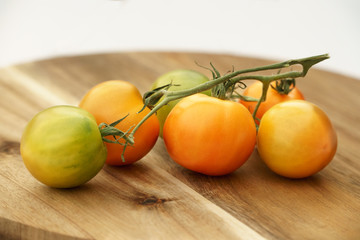 Unripe green, orange and yellow tomatoes on wooden board
