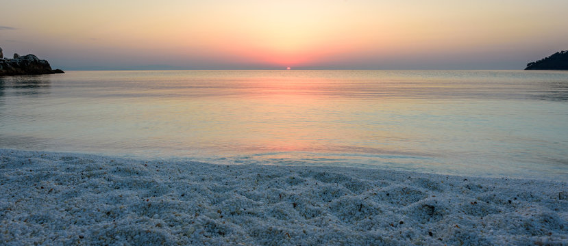 Beautiful summer sunrise at Marble beach on Thassos island - calm water, pink skies, white marble pebbles in the foreground - perfect vacation spot