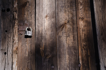 Small iron lock on metal fastener hangs on high wooden gate