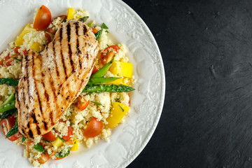 couscous salad with grilled chicken and asparagus on white plate. stone table. healthy food