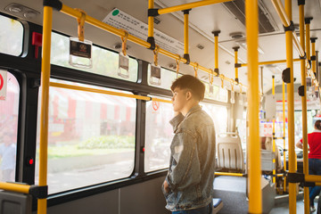 Asian man taking public transport, standing inside bus. © makistock