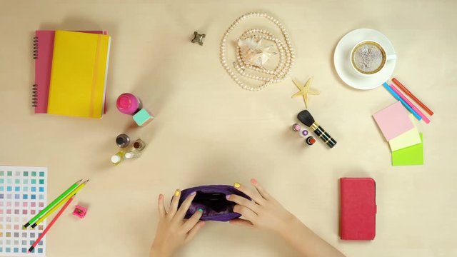 Top view of woman's dresser desk, hands gathering cosmetics in purse, lifestyle. Colorful objects on woman's desk