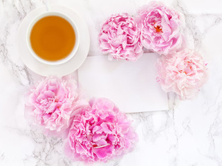 Tea time. Flat lay over light background with peonies and cup of tea. Copy space for thr text
