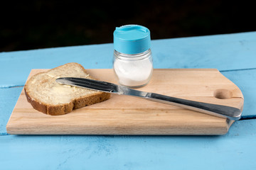 Flat lay butter spread on bread with knife and saltshaker served on a wooden board