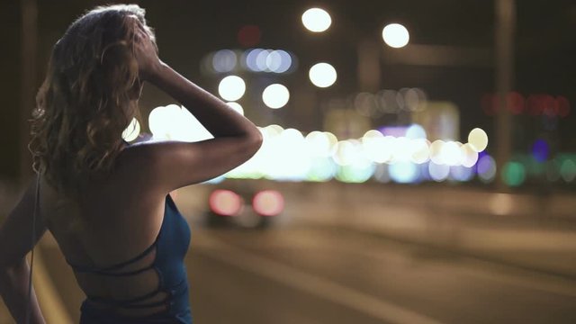 prostitute is standing on the side of the night road where the lanterns are shining and waiting for the client