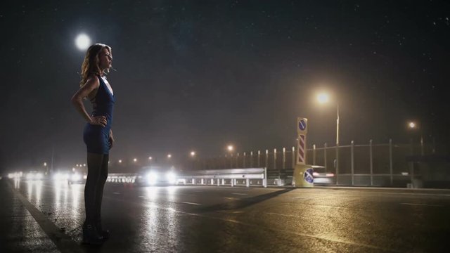 prostitute is standing on the side of the night road where the lanterns are shining and waiting for the client