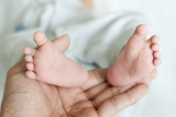 An adult man is holding the feet of a newborn