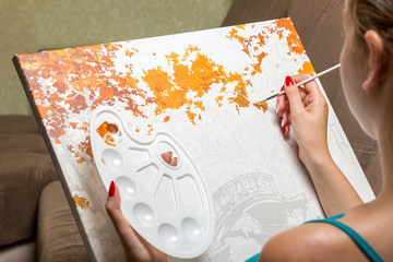 Young girl draw with a brush painting by numbers on canvas. The concept of a hobby