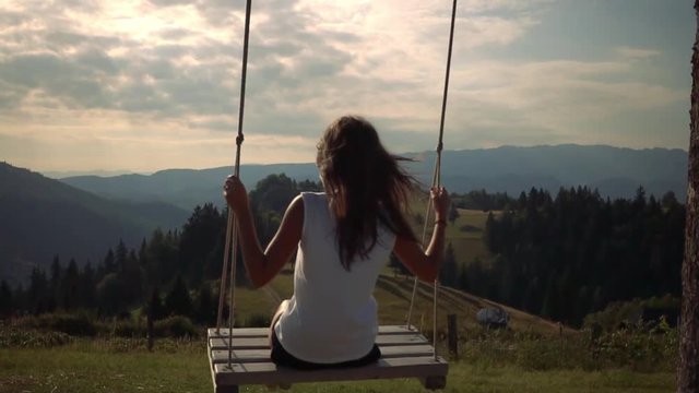 Young girl in swing in front of great mountain view - slow motion