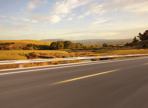 Asphalt road beside grassland at sunset