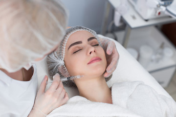 Hands of cosmetologist making injection in face, lips. Young woman gets beauty facial injections in salon. Face aging, rejuvenation and hydration procedures. Aesthetic cosmetology.