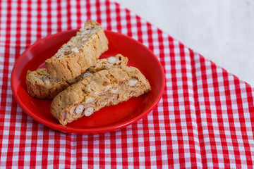 Cantucci. Typical Italian cookies on a saucer of red color and on a white wooden background
